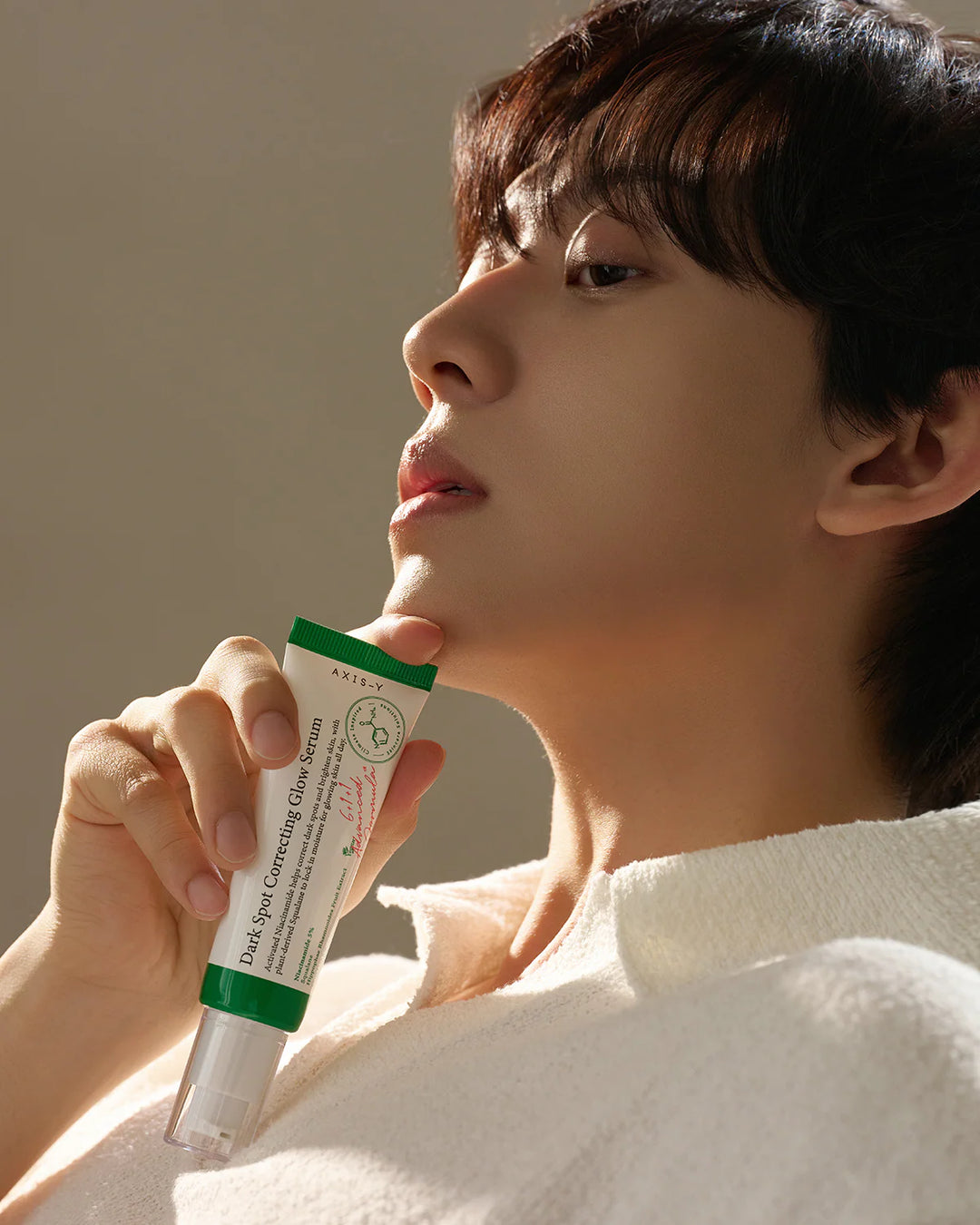 Model holding AXIS-Y Dark Spot Correcting Glow Serum bottle for fading hyperpigmentation and acne scars